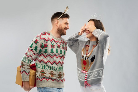 圣诞毛衣摄影照片_人和假日概念—在丑毛衣党的快乐夫妇的肖像与圣诞礼物。快乐的夫妇在圣诞毛衣与礼品盒