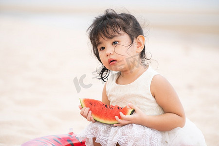 吃女孩西瓜摄影照片_夏天，可爱的孩子在热带沙滩上吃西瓜。可爱的孩子在海滩上吃西瓜。