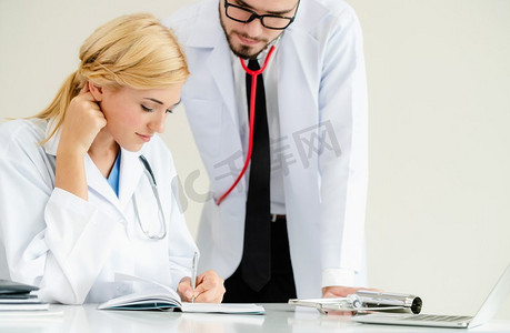 医院办公室的医生在与站在她旁边的另一名医生交谈时，在病人报告上写下了笔记。