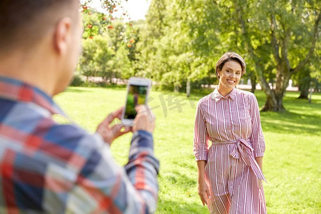 手机夏季夏季摄影照片_人，技术和生活方式的概念—快乐的夫妇拍摄智能手机在夏季公园。夫妇拍摄通过智能手机在公园