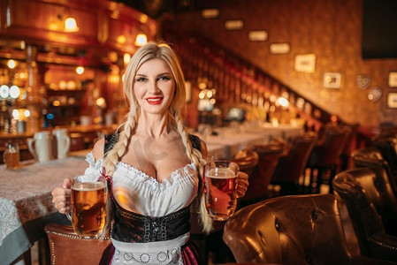 性感的女服务员在酒吧里拿着两杯新鲜啤酒。有吸引力的形状的酒吧女招待。性感的女服务员举行两杯新鲜啤酒在酒吧