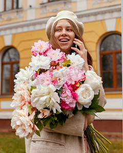 时尚的微笑的妇女拿着花束鲜花户外春天说话的电话