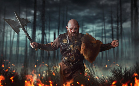 愤怒的维京人与斧头穿着传统的北欧衣服战斗在火，战斗在森林。斯堪的纳维亚古代战士