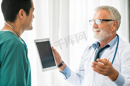 资深男医生在医院与另一位医生讨论时使用平板电脑。医护人员和医生服务。