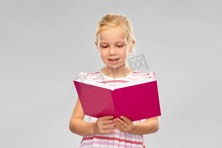 童年与人的概念--灰色背景下微笑的小女孩看书。微笑的小女孩看书