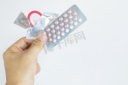 避孕手段:女人手拿着避孕药和避孕套在床上.
