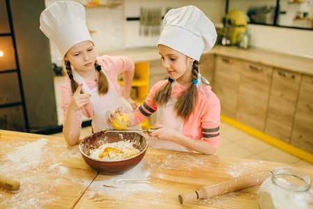 两个小女孩厨师在帽子擦柠檬到碗，饼干准备在厨房。孩子们在做糕点，孩子们在做蛋糕
