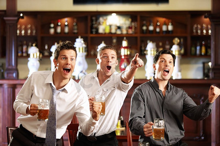 男性观众摄影照片_三个拿着啤酒的男人在酒吧里为他们最喜欢的球队的胜利而欢呼