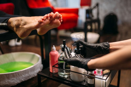 修脚浴后戴黑手套的修脚师做足部按摩，美容院的女顾客。专业指甲护理，足部按摩