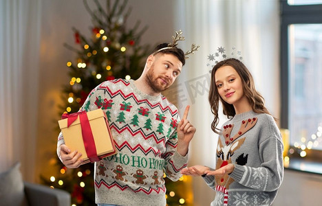 人和假日概念—在丑毛衣党的快乐夫妇的肖像与圣诞礼物。快乐的夫妇在圣诞毛衣与礼品盒