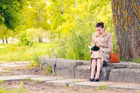 在一个阳光明媚的春日，一位优雅的女商人坐在石墙上，读着一本冒险小说