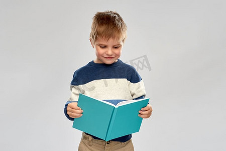 童年和教育概念—微笑的小男孩读书在灰色背景。微笑的小男孩读书
