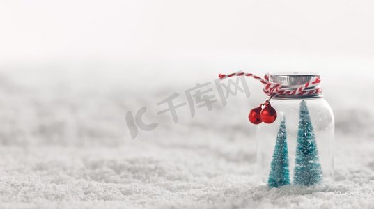 玻璃罐的圣诞装饰品与条纹丝带，铃铛和冷杉树里面在雪背景。圣诞装饰品在雪地上