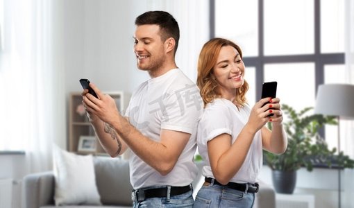 技术和人的概念—在白色T恤与智能手机在家庭背景的快乐夫妇。快乐的夫妇在白色T恤与智能手机