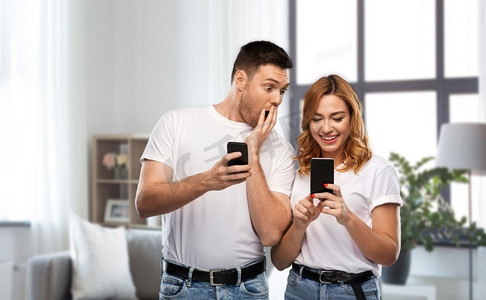 与人连接摄影照片_技术和人的概念—在白色T恤与智能手机在家庭背景的快乐夫妇。快乐的夫妇在白色T恤与智能手机