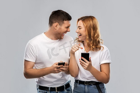 技术和人的概念—愉快的夫妇在白色t恤与智能手机在灰色背景。快乐的夫妇在白色T恤与智能手机