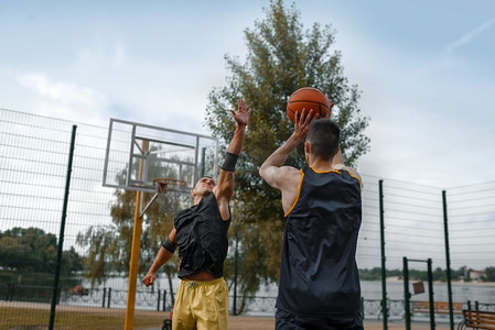 两名篮球运动员在户外球场上打球。身穿运动服的男运动员在公园里进行街球训练