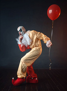 疯狂钜惠摄影照片_疯狂的血腥小丑与化妆狂欢节服装持有气球，疯狂的疯子，可怕的怪物。狂欢节服装血腥小丑举行气球