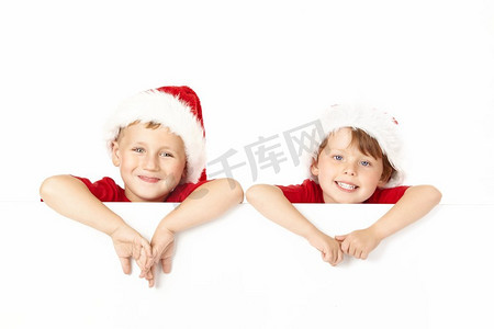两个戴着圣诞老人帽子的小男孩靠在隔绝的空白横幅上