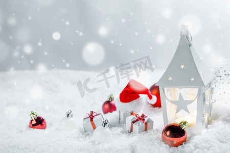 蓝色元宵灯笼摄影照片_圣诞节节日卡与礼物，球，圣诞老人帽子和发光灯笼在雪。圣诞装饰在雪