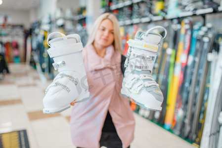 一名妇女在体育用品店展示白色滑雪或滑雪靴。冬季极端的生活方式，积极休闲，女性客户与保护设备