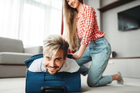 快乐的女孩把她丈夫装进行李箱里。关于假期概念的费用。快乐的女孩把她的丈夫装在手提箱里