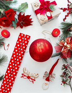 红色的圣诞装饰品和白色桌子上的包装纸，上面有冷杉树枝和圣诞花。俯视图。平铺