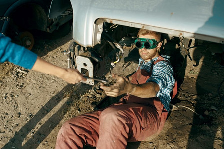 在汽车垃圾场焊接眼镜的男性机械师。合照美女