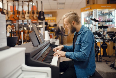 买手店摄影照片_一名男性音乐家在音乐商店里试着弹钢琴。乐器店的杂货，键盘手购买设备，市场上的钢琴家