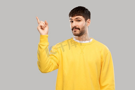 人物概念--穿着黄色运动衫的年轻人用手指指着灰色背景上的东西。一名男子将手指指向某物