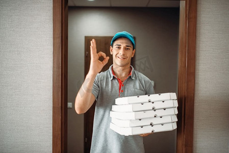 快活的披萨外卖小哥表示OK符号，正在送货服务。披萨店的快递员将纸板包裹放在室内