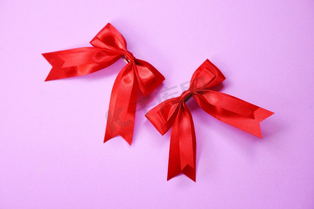 蝴蝶结丝带摄影照片_在粉红色背景的红丝带蝴蝶结/两个礼物蝴蝶结发夹完美的假日手工制作