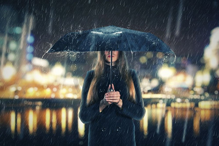 一名女子在夜里撑着黑色的雨伞站在雨中