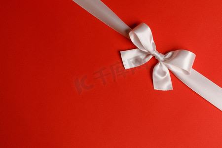 白色缎子丝带蝴蝶结在红纸背景。红色的白色蝴蝶结