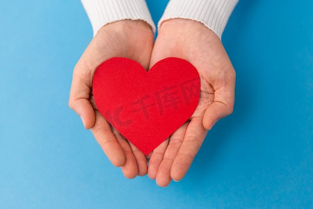 爱，健康和情人节概念—手持红色心形在蓝色背景。’手拿着红色心形在蓝色背景