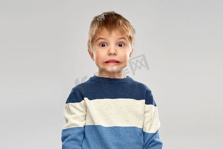 童年，表达和人的概念—震惊的小男孩在条纹套衫在灰色背景。穿着条纹套衫的震惊的小男孩