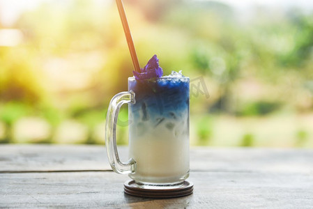 加冰饮品摄影照片_蝴蝶豌豆饮品木杯，自然绿底/冰蓝豌豆花加奶汁夏日