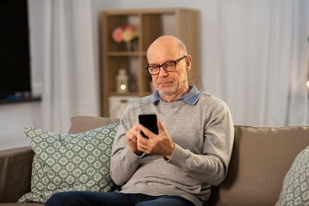 技术，人和通信概念—秃头高级男子发短信在智能手机在家里晚上。高级男子在家里的智能手机上发短信
