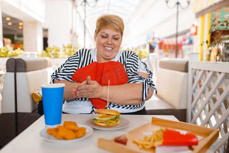胖女人在商场美食广场准备吃快餐。在餐桌旁吃垃圾午餐的超重女性