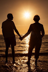 年长的男人和女人夫妇牵手在日落或日出在一个废弃的热带海滩 