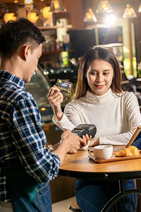 一位亚洲顾客在咖啡馆的餐桌上用非接触式nfs技术向服务员支付购买咖啡的费用。
