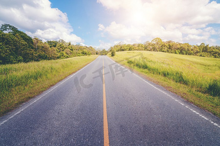 公路上山通过绿色的草地在白云下在蓝天在夏天。公路旅行的概念。