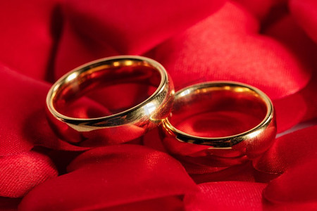 枚红色摄影照片_两枚金色结婚戒指以红色缎子心形为背景。红色的金色结婚戒指