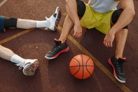 两个篮球运动员坐在室外球场的地上。男子运动员在街球训练后穿着运动服