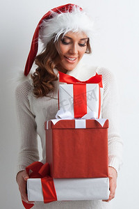 微笑的可爱的女孩在圣诞帽与红色圣诞礼物盒。女孩与圣诞礼物盒