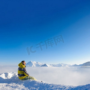 雪摄影照片_高山冬季山风景与人坐在低云之上。法国阿尔卑斯山在晴天被雪覆盖。Val—d Isere’