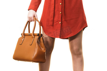 时尚的不可识别的妇女拿着皮包呈现时尚的配件。女性持棕色皮包