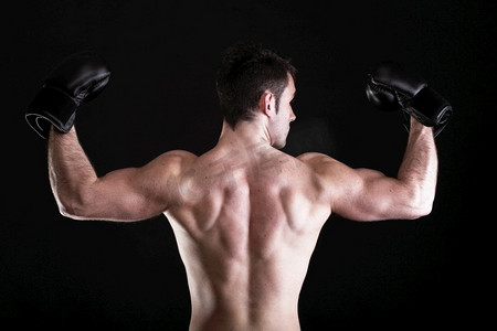 健身运动男摄影照片_拳击手举起手臂强壮的运动肌肉男，运动男展示肌肉男性背部孤立在黑色背景下