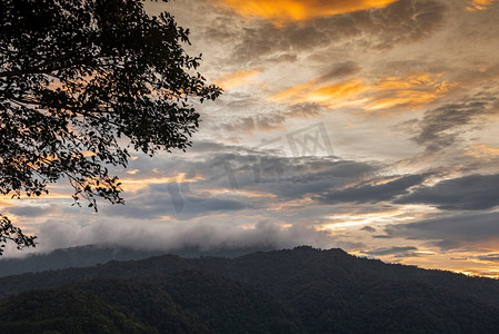 橙色风景摄影照片_日落风景美丽的橙色天空云在有树前景的山/日落山森林雾雾在亚洲