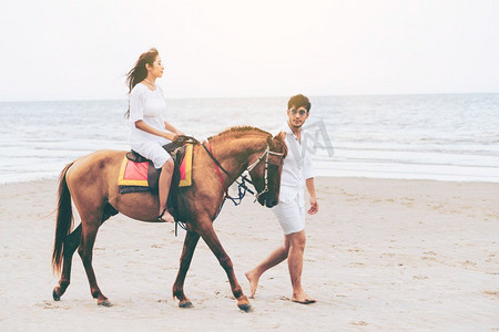 在蜜月旅行假期期间走在海滩上的愉快的年轻夫妇。年轻夫妇在热带海滩骑马。